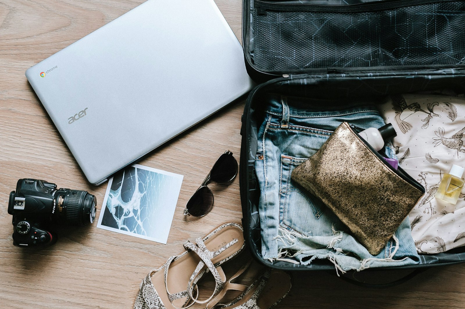Open suitcase flat lay with clothes, camera and sunglasses arranged on a wooden floor