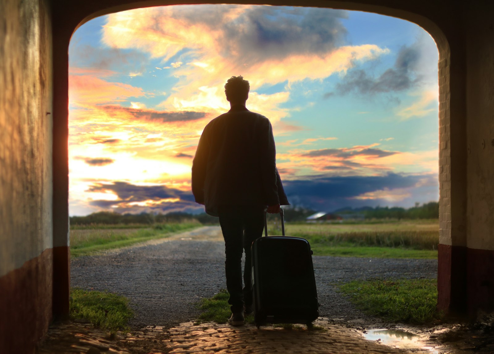 Traveler with a rolling suitcase silhouetted against a dramatic sunset