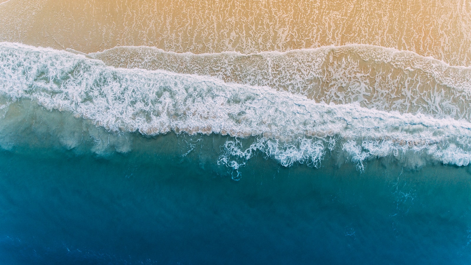 Aerial view of turquoise Gulf water and white surf rolling onto the sand